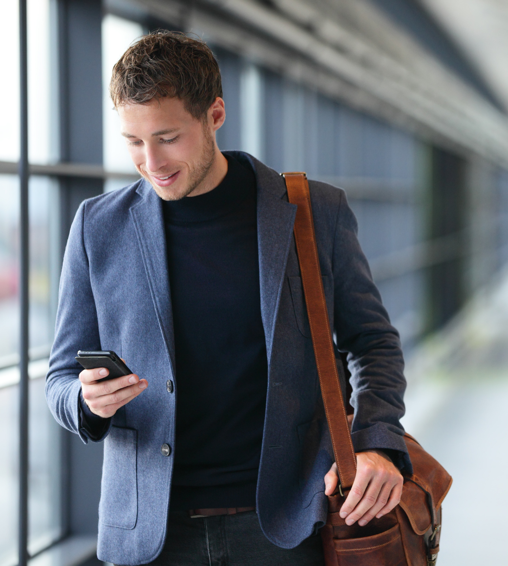A professional man smiling while checking his smartphone in a modern public space.